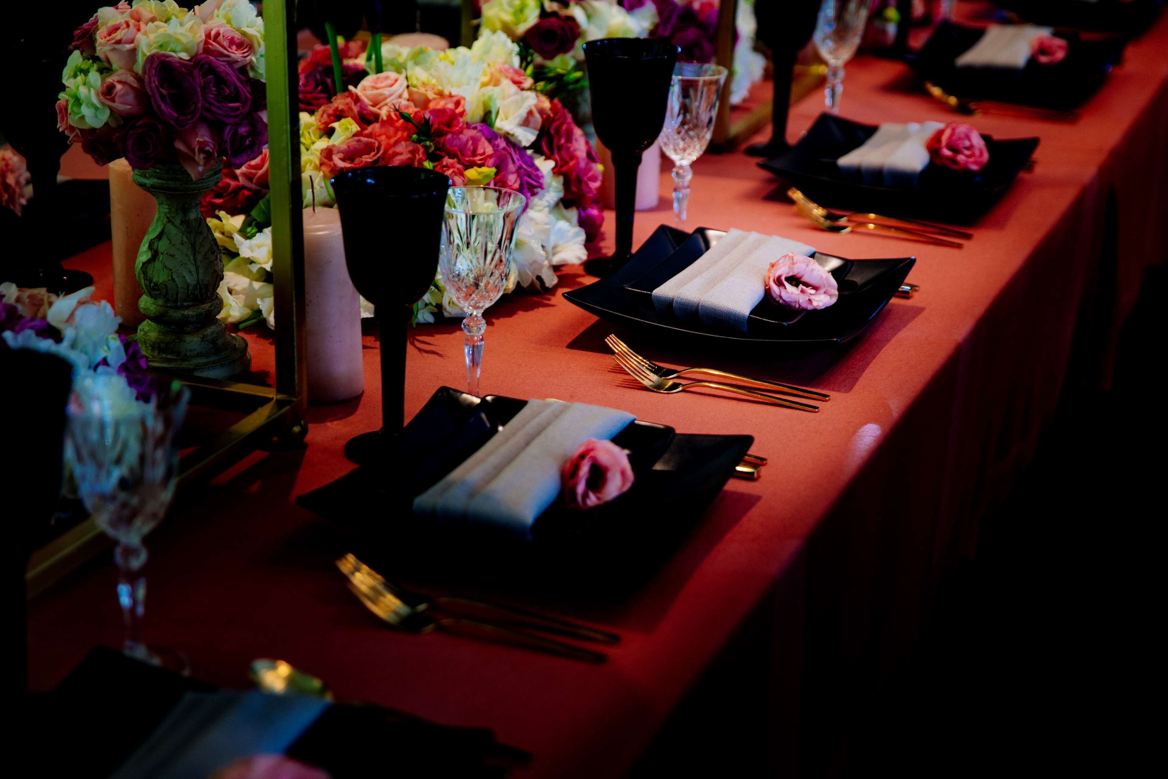 Una mesa dispuesta para una cena formal, con platos negros, servilletas dobladas y un jarrón de flores.