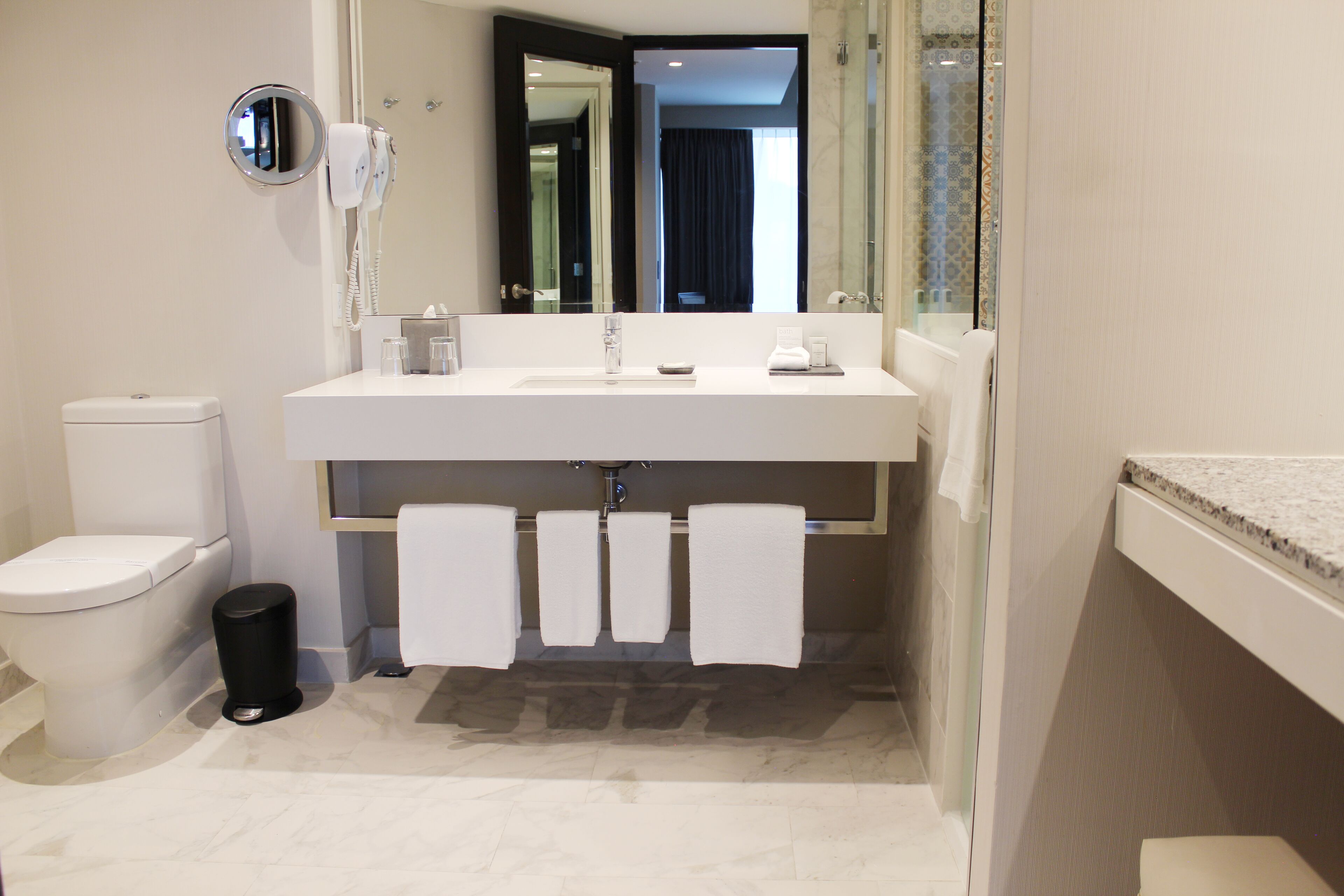 Un baño moderno con un lavabo blanco, un inodoro, un cubo de basura y un espejo.