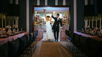 Una ceremonia de boda con una novia y un novio caminando por el pasillo, rodeados de arreglos florales y mesas dispuestas para los invitados.