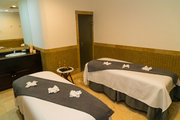 A hotel room with two beds, a bathroom with a sink, and a small table with toiletries.