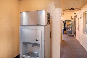 Un distributeur de boissons compact et métallique, doté d’un système de refroidissement de l’eau, est installé dans un couloir dont le mur présente une texture particulière, avec un distributeur automatique en arrière-plan.