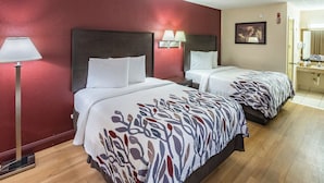 A hotel room with two beds, a nightstand, a lamp, a painting, and a bathroom with a sink and mirror.
