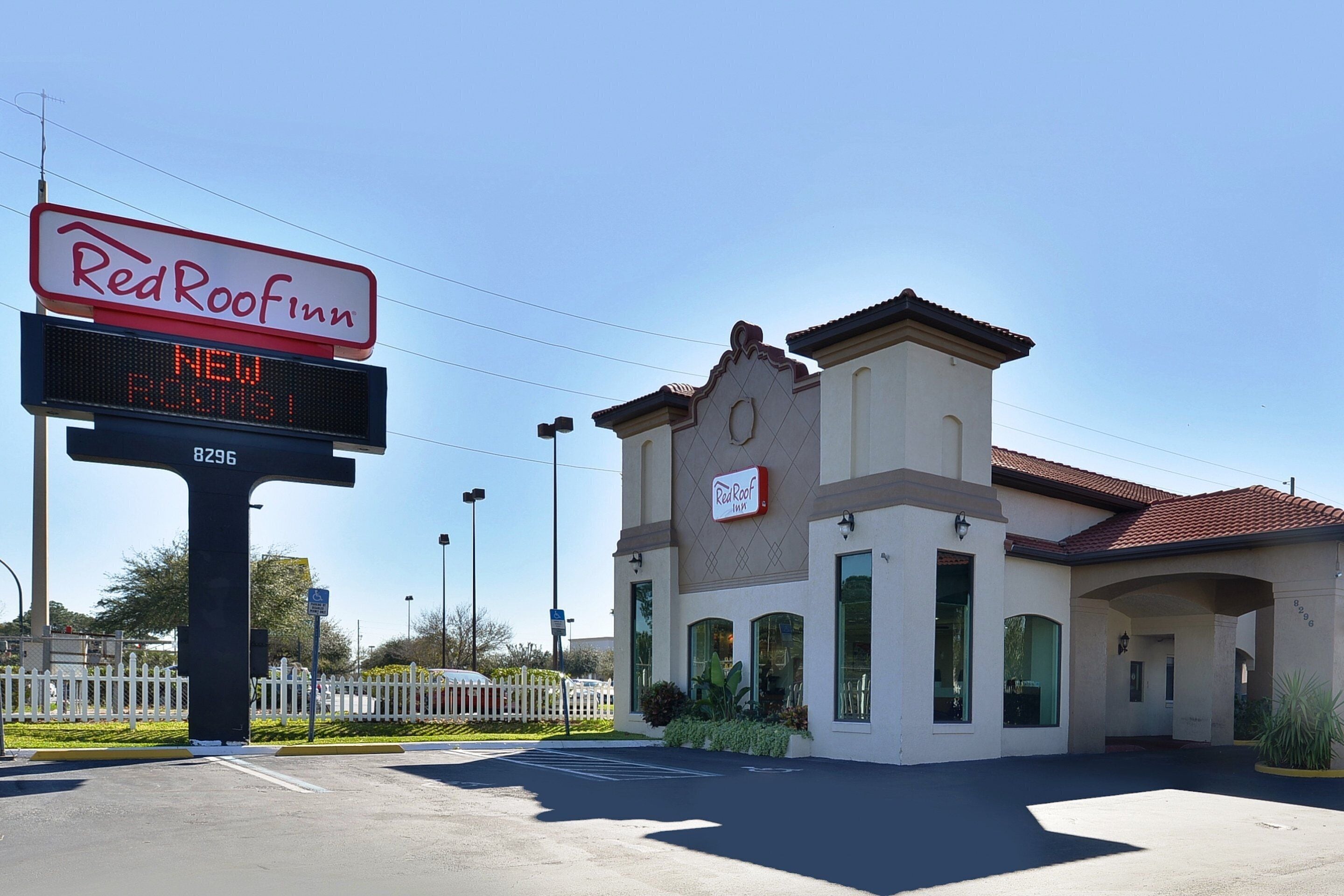 A Red Roof Inn with a digital signboard, a gated parking area, and a building with a traditional architectural style.