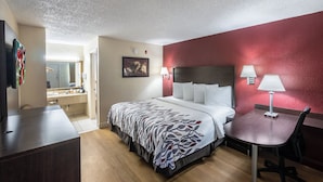 Habitación de hotel con cama, escritorio, silla y baño visible a través de una puerta abierta.