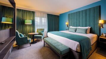 A hotel room with a large bed, a bench, a chair, a small table, and a mirror.