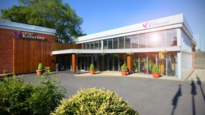 A modern hotel with a prominent sign, large windows, and potted plants in front. - Hotel Killarney (Killarney)