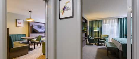 Une chambre d’hôtel avec un canapé, des fauteuils, un téléviseur, un tableau encadré et un lit.