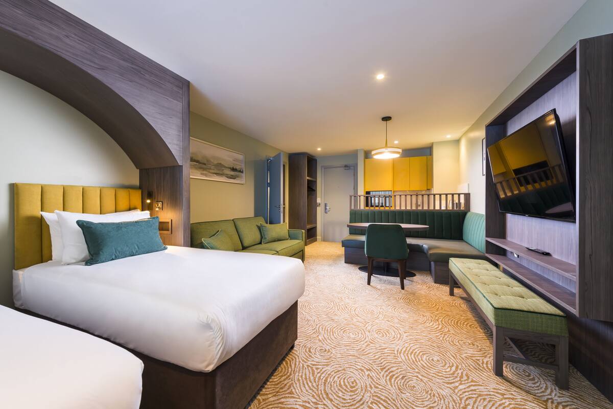 A hotel room with a large bed, a sofa, a bench, a desk, and a TV.