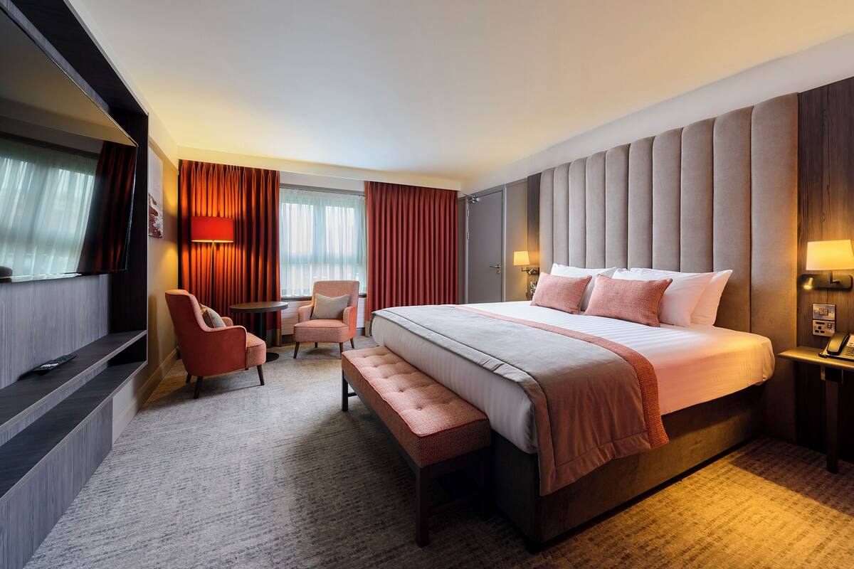 A hotel room with a large bed, a desk, a chair, and a TV.