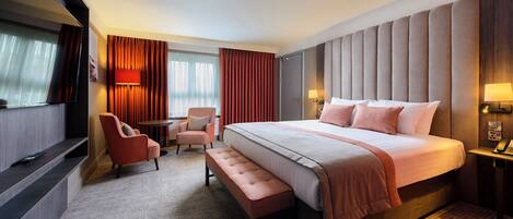 A hotel room with a large bed, a desk, a chair, and a TV.