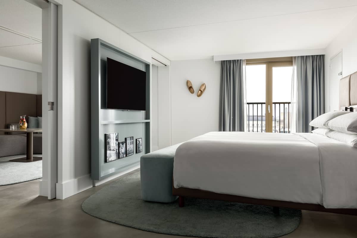Une chambre d’hôtel moderne dotée d’un grand lit, d’une télévision à écran plat, d’un coin salon avec une table et des chaises, et d’un balcon avec des rideaux.