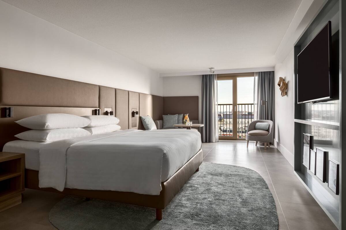 Une chambre d’hôtel moderne dotée d’un grand lit, d’une télévision à écran plat, d’une petite table d’appoint, d’une chaise et d’un balcon avec vue.