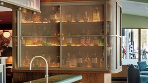 Una zona de bar con mostrador de mármol, una vitrina de vidrio con botellas y un área de estar con sillas amarillas.