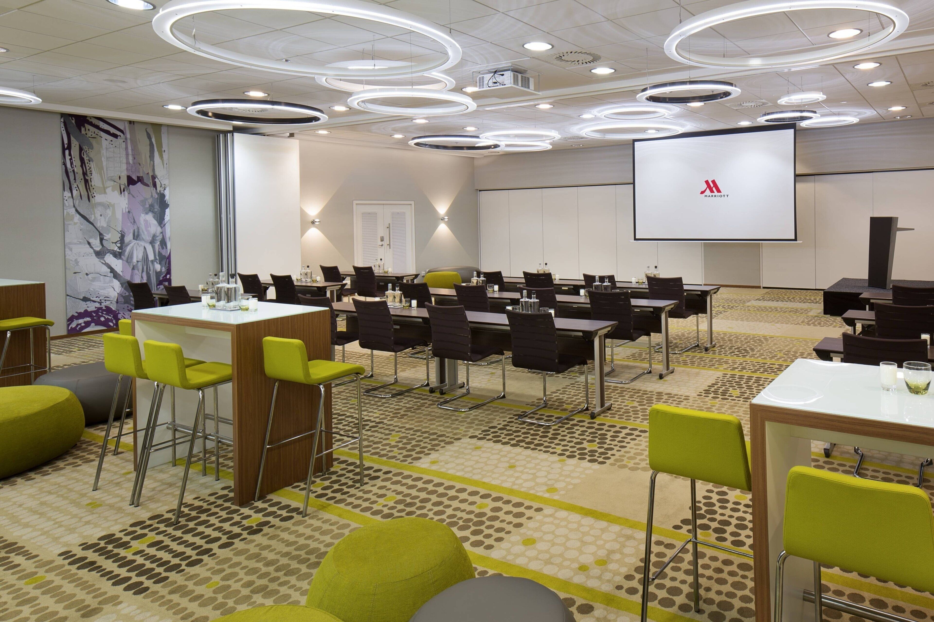 A conference room with a large screen, multiple tables, and chairs.