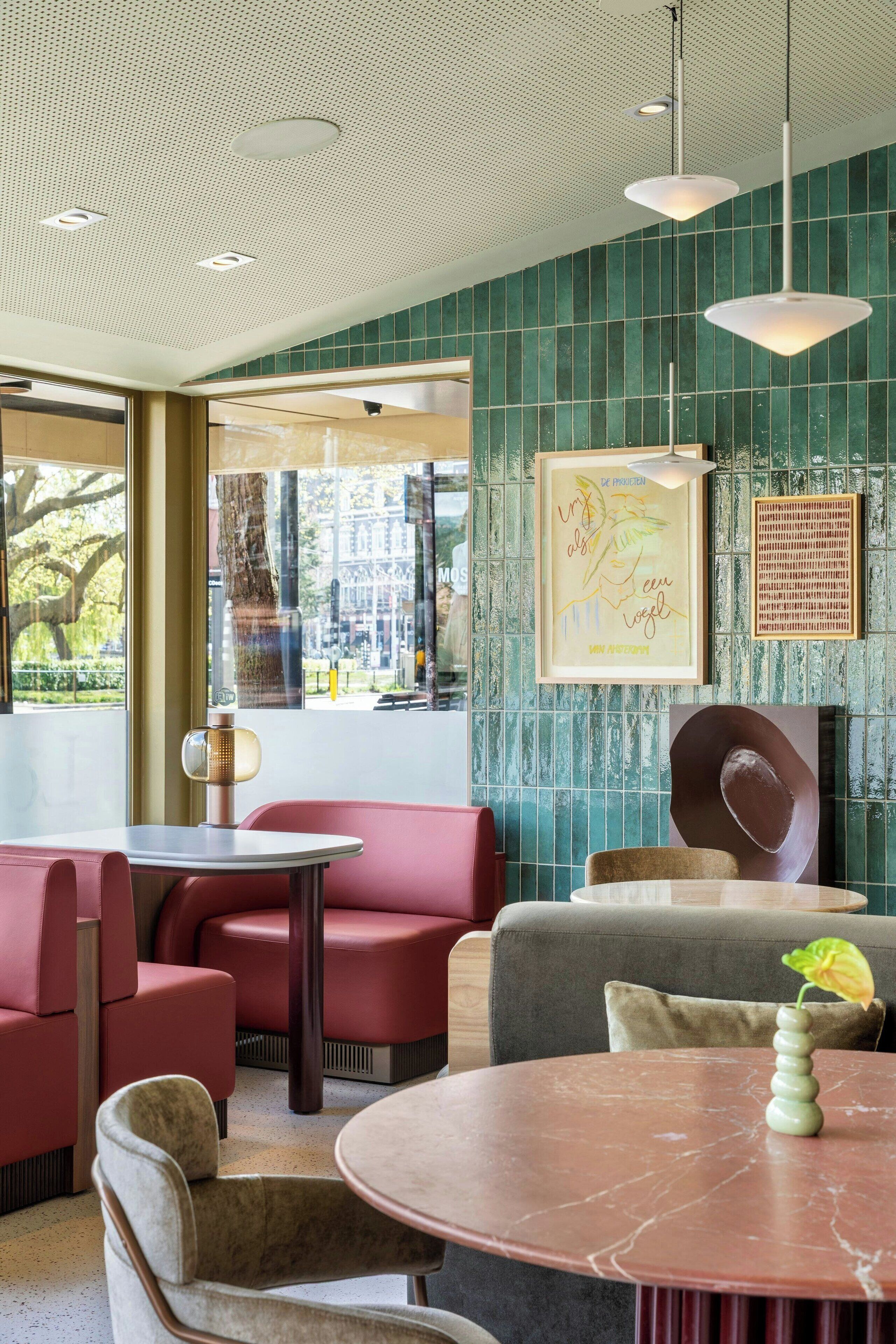 A modern interior with teal tiled walls, red seating, and a marble table with a vase.