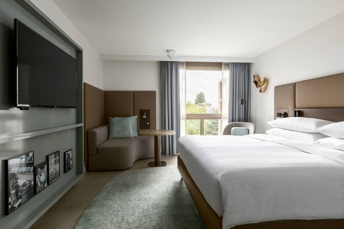 Une chambre d’hôtel avec un grand lit, un canapé, une petite table et un téléviseur fixé au mur.