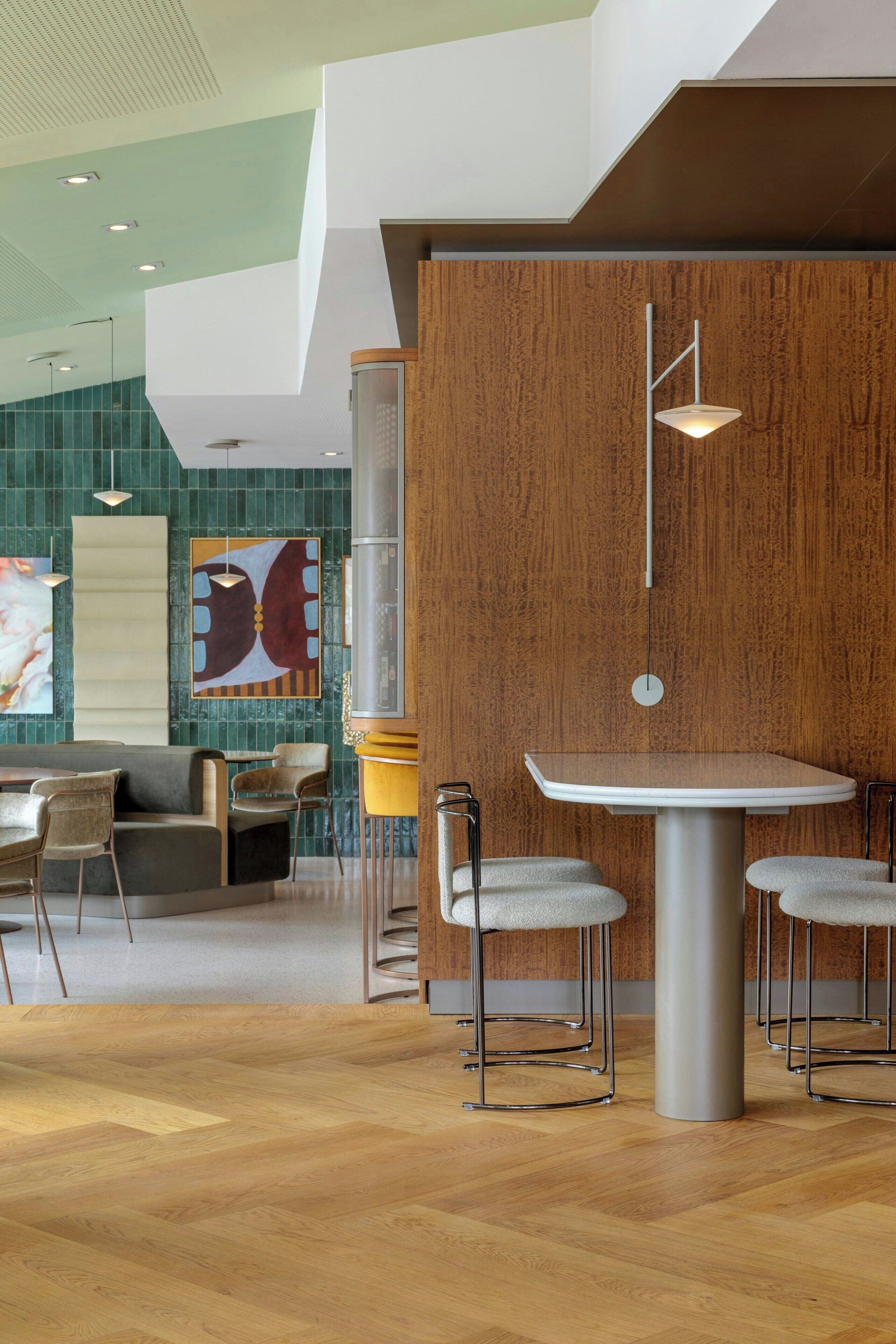 A modern interior with a round table and bar stools, a wooden accent wall, and a large abstract painting.