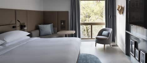 Una habitación de hotel moderna con una cama grande, una zona de estar con una silla, una mesita y un televisor en la pared.