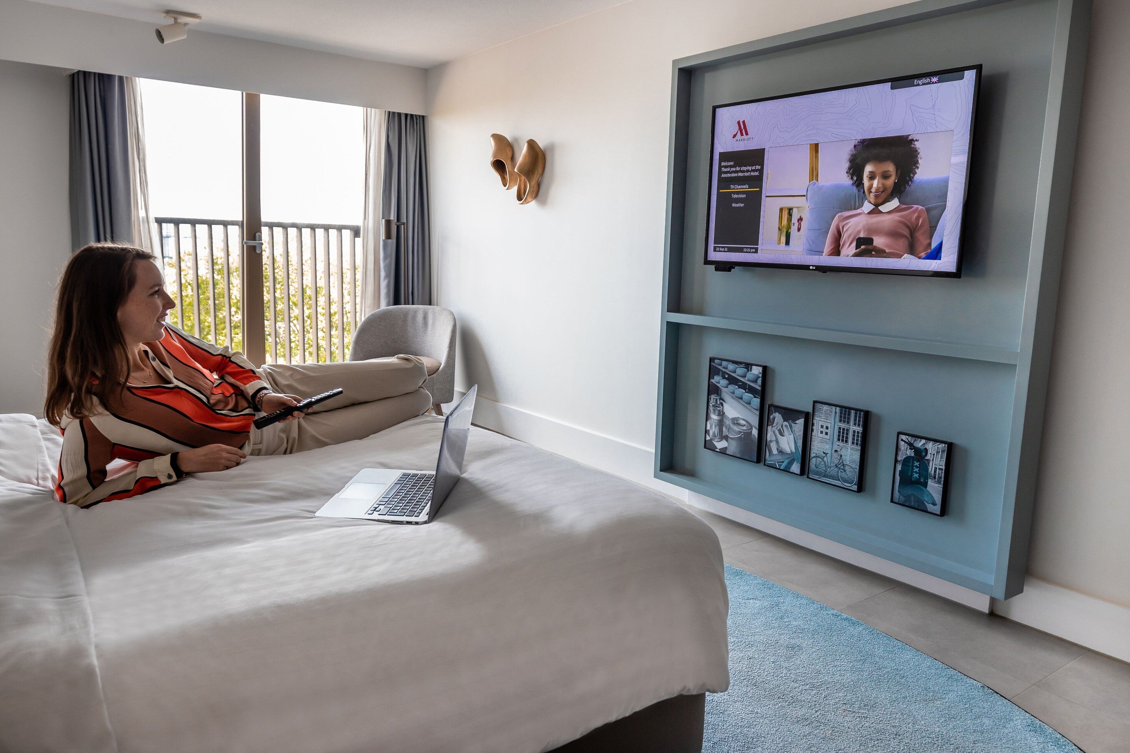A hotel room with a bed, a laptop, a television, and a framed picture collection on the wall.