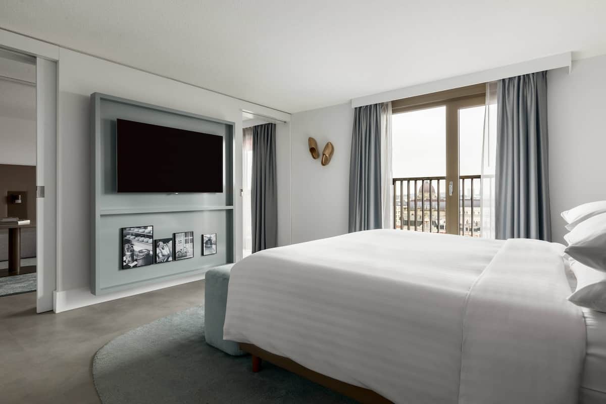 Une chambre d’hôtel moderne dotée d’un grand lit, d’un téléviseur à écran plat fixé au mur et d’un balcon avec des rideaux.