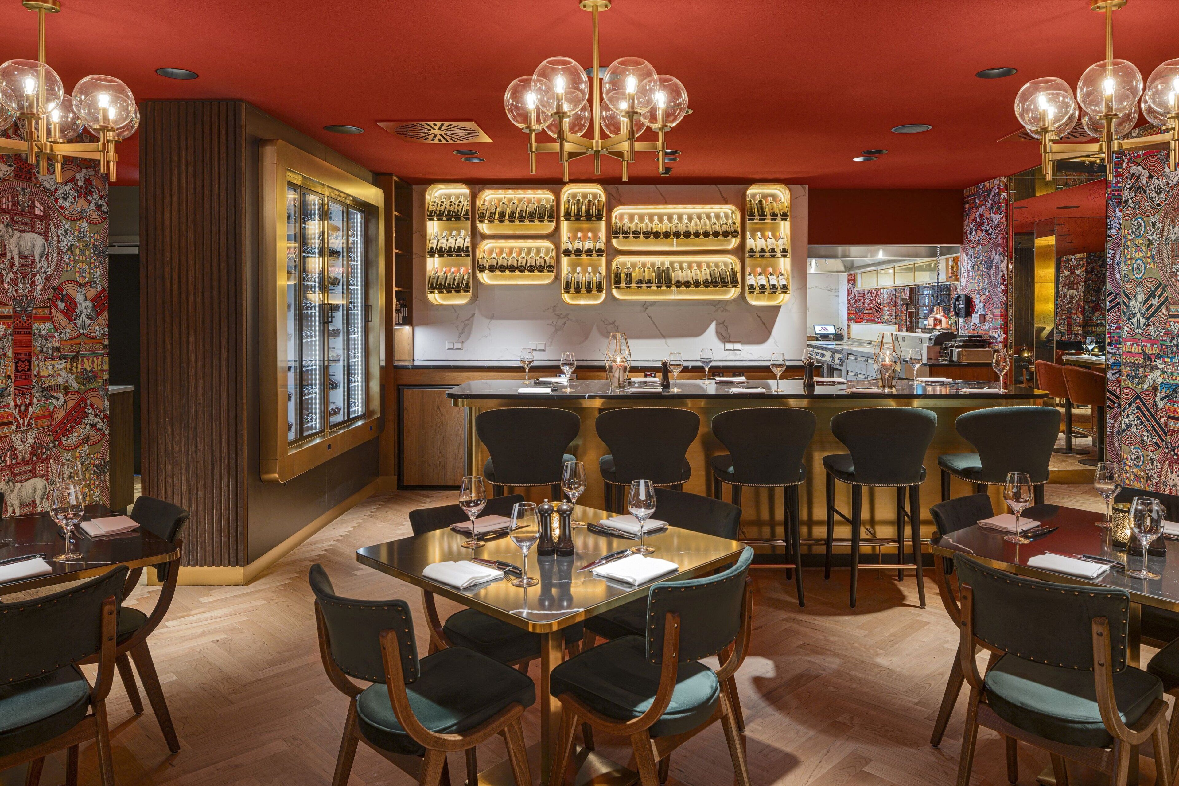 A restaurant with multiple tables and chairs, a bar area, and a decorative wall with a pattern.