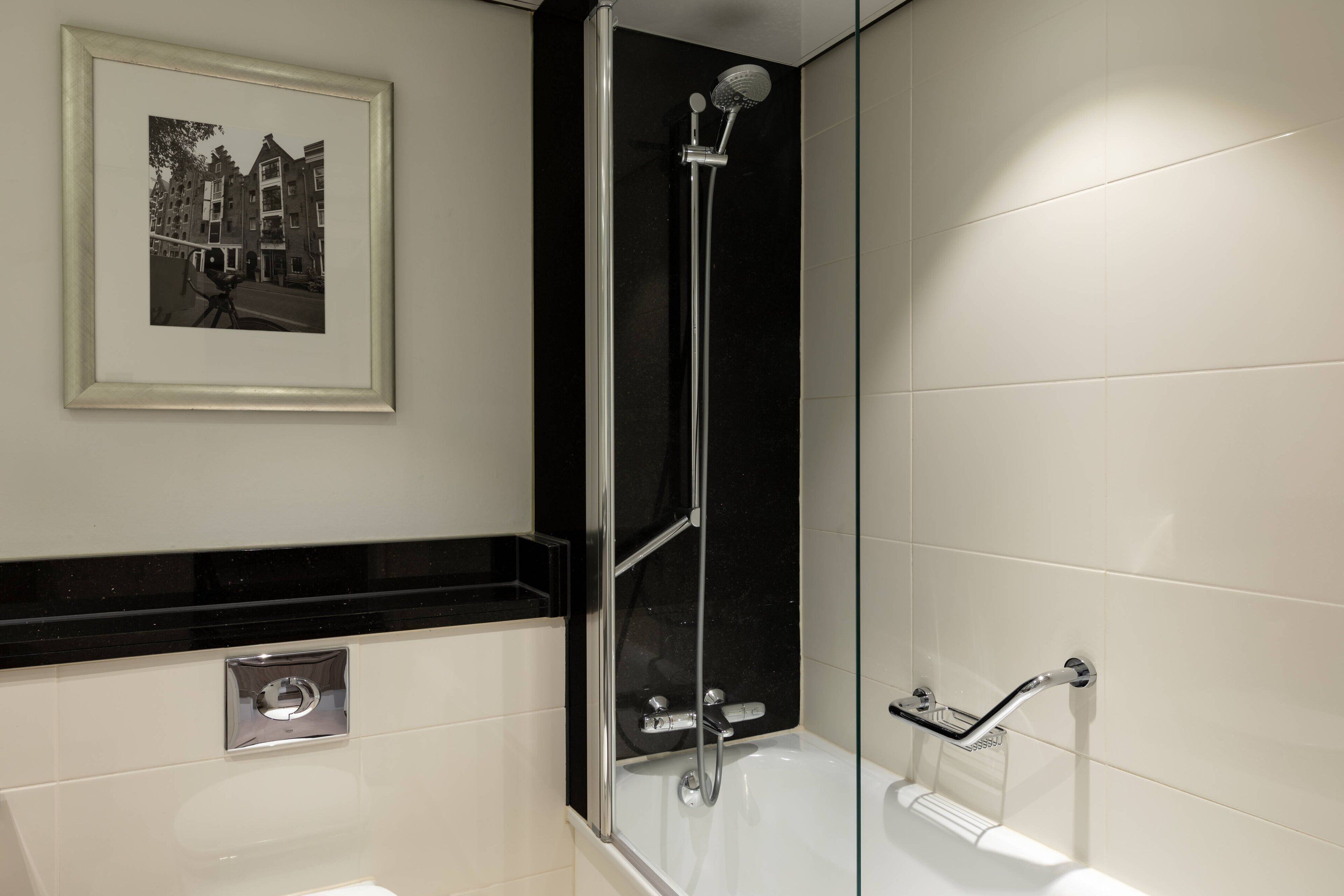 A modern bathroom with a glass-enclosed shower, a framed photograph on the wall, and a black countertop.