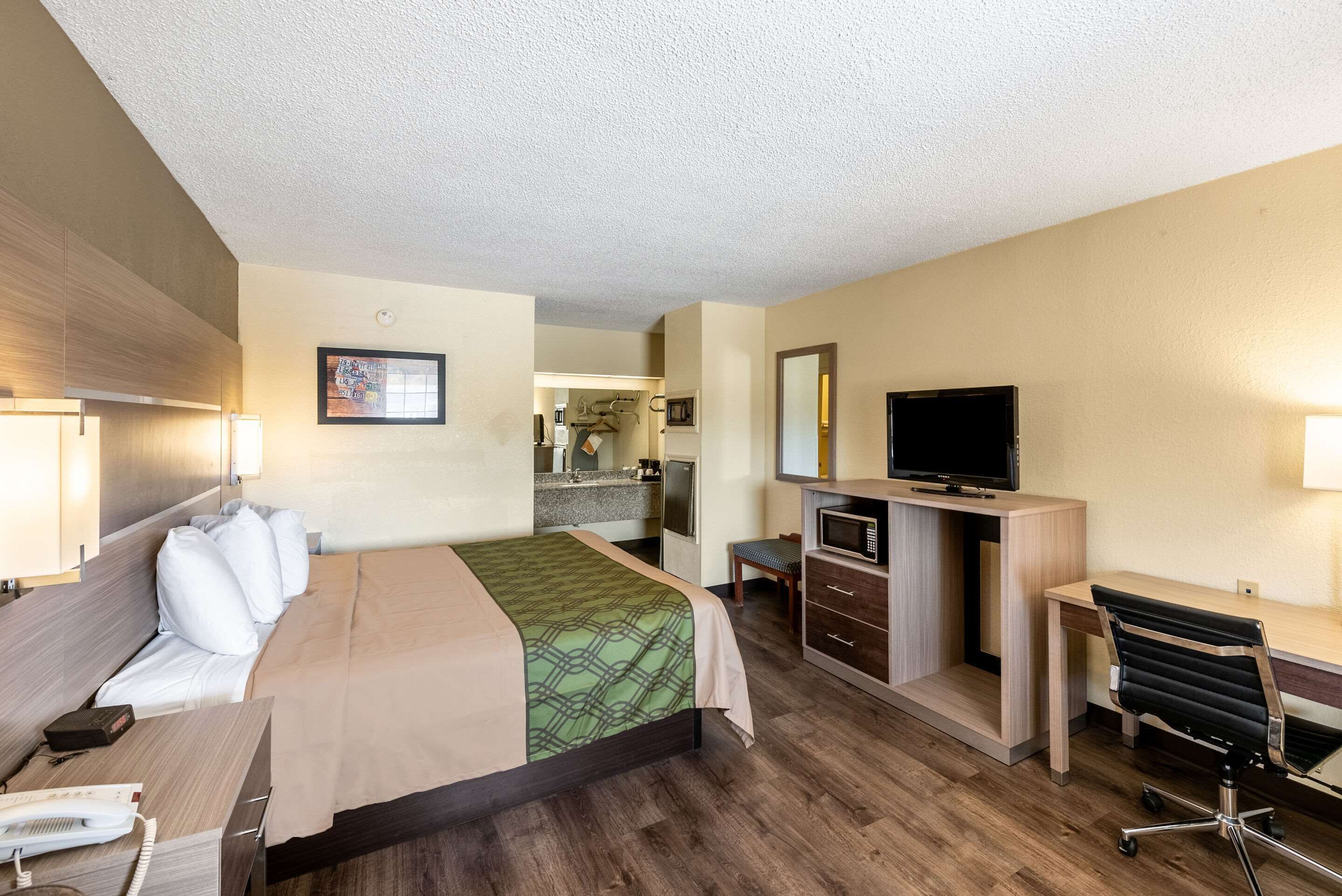 A hotel room with a bed, desk, chair, TV, and kitchenette.