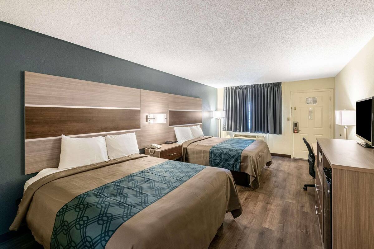 A hotel room with two beds, a desk, a television, and a door.