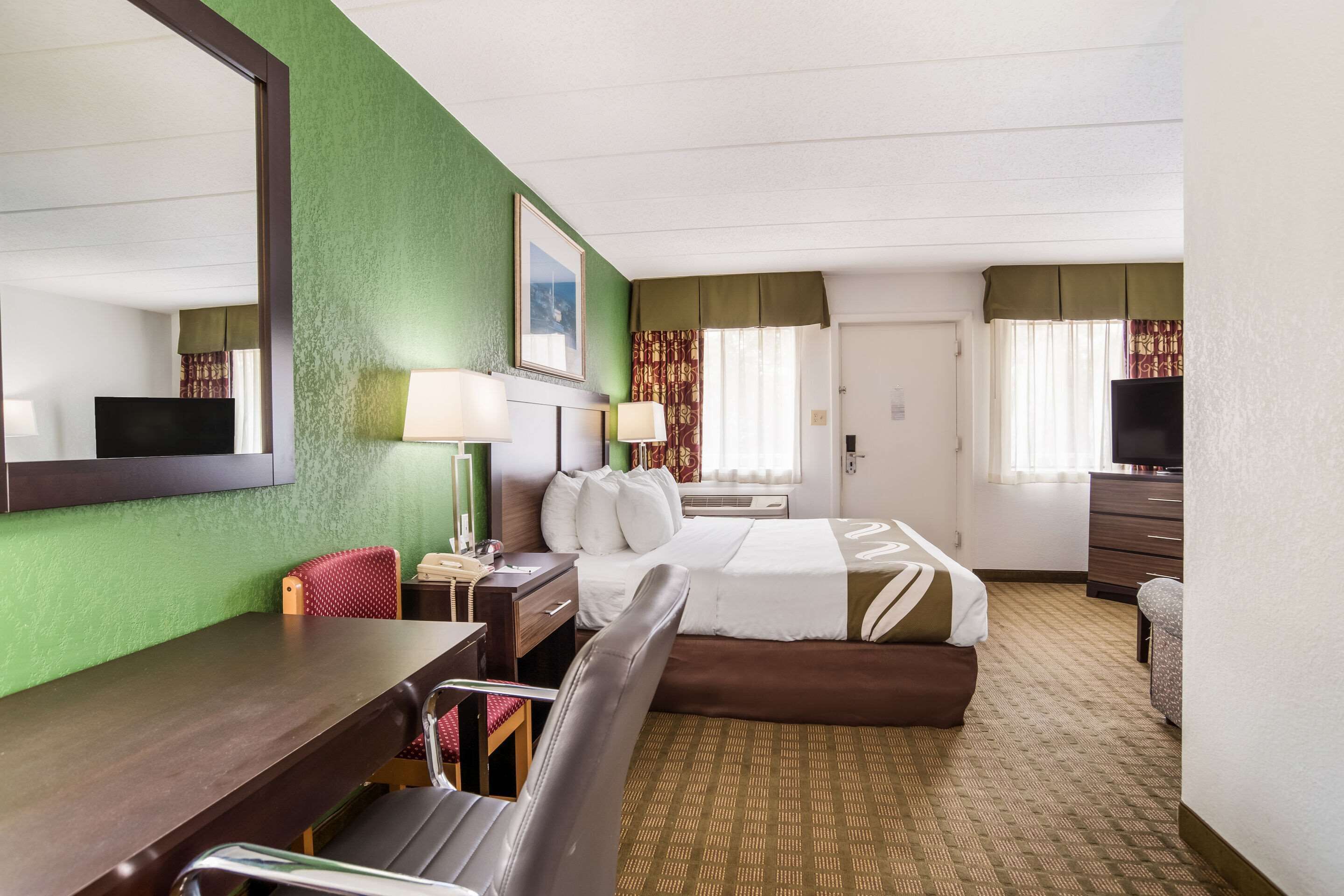 Une chambre d’hôtel avec un lit, un bureau, une chaise, une télévision et une fenêtre avec des rideaux.
