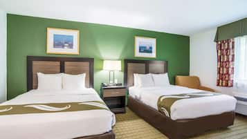 Une chambre d’hôtel avec deux lits, des murs verts, des tableaux encadrés, une table de chevet, une lampe et une fenêtre avec des rideaux.