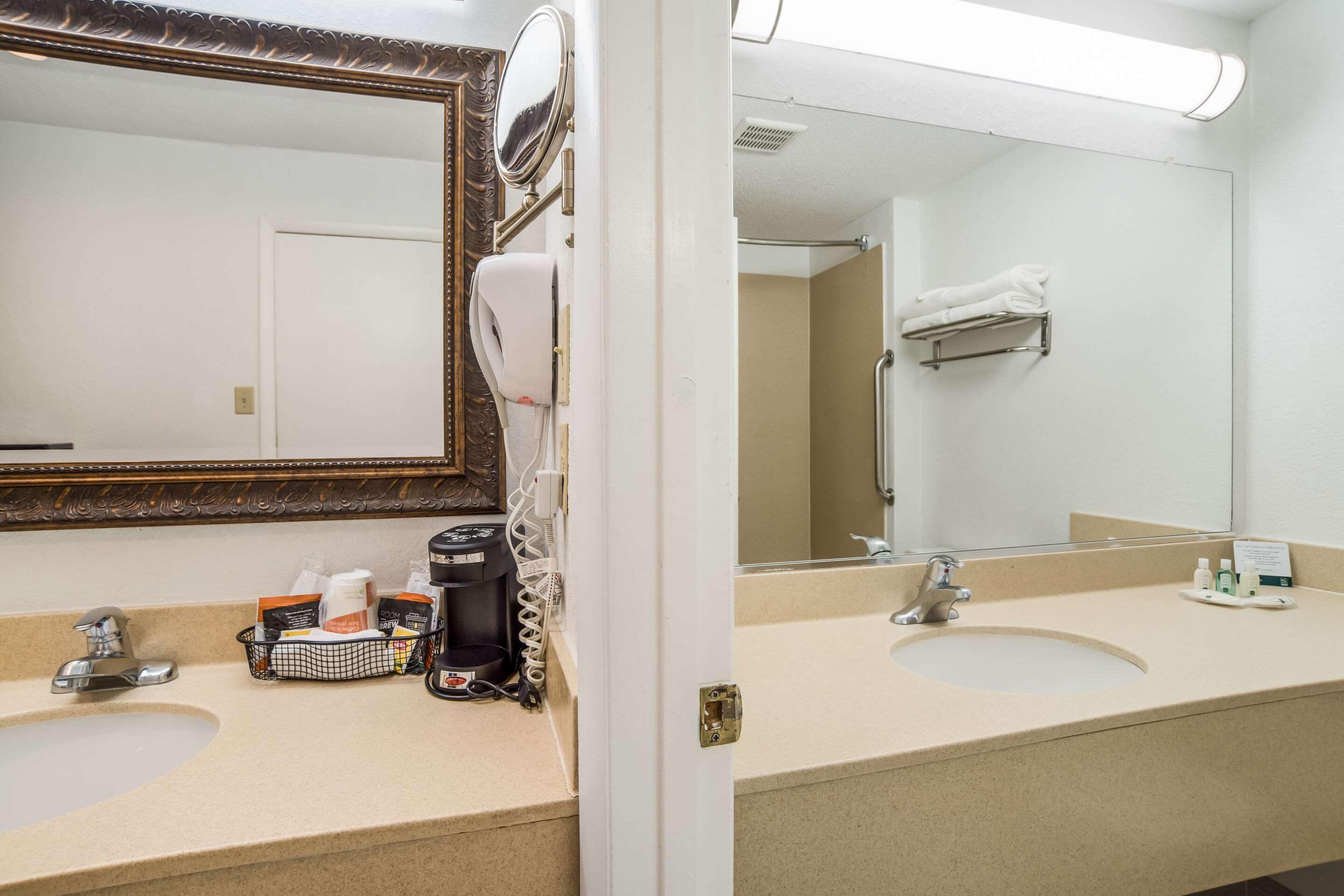 Un baño de hotel con dos lavamanos, un espejo grande, un secador de pelo y un perchero para toallas.