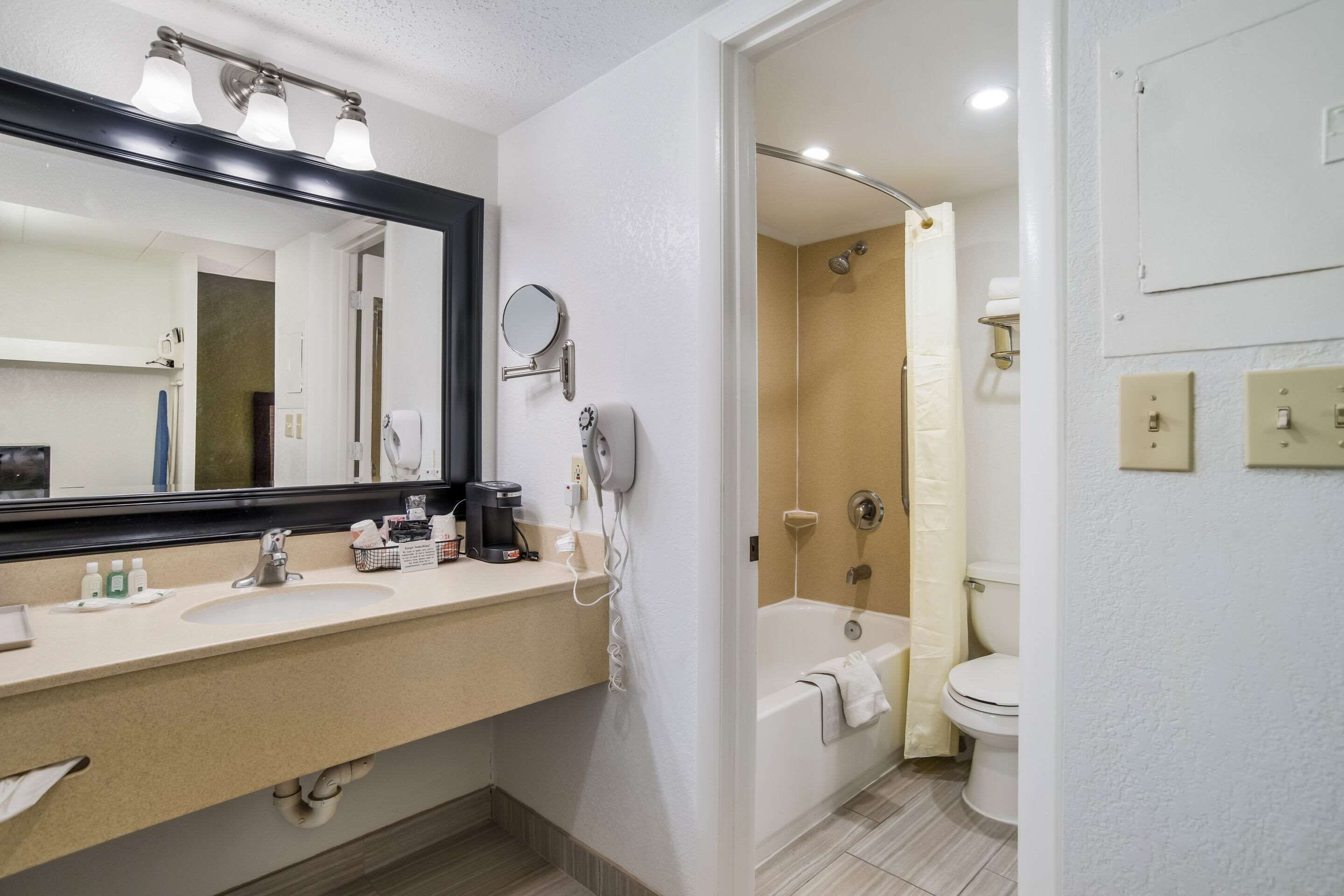 A modern bathroom with a large mirror, two sinks, a shower, and a toilet.
