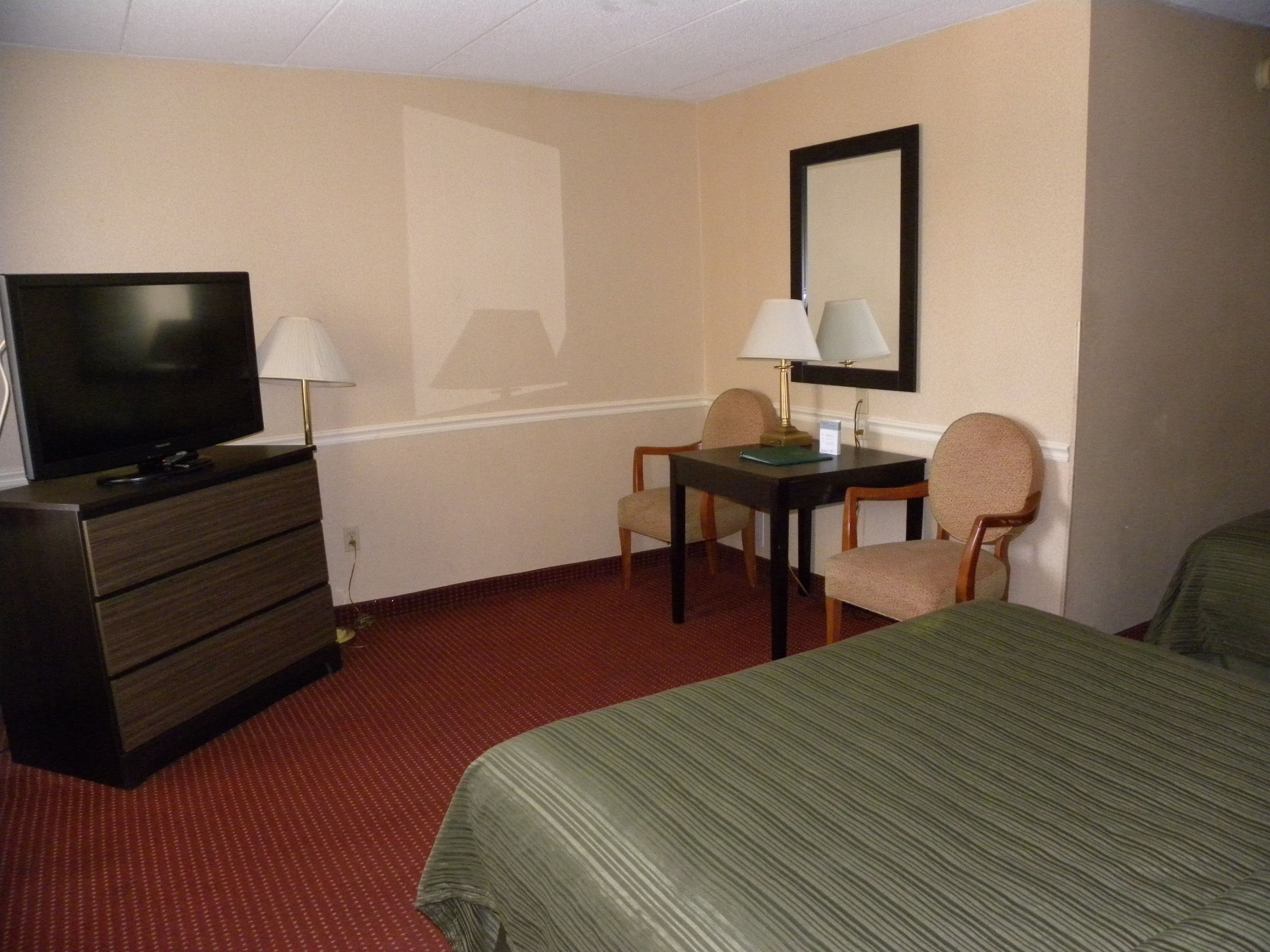 A hotel room with a bed, a TV on a dresser, a desk with a chair, and a lamp.