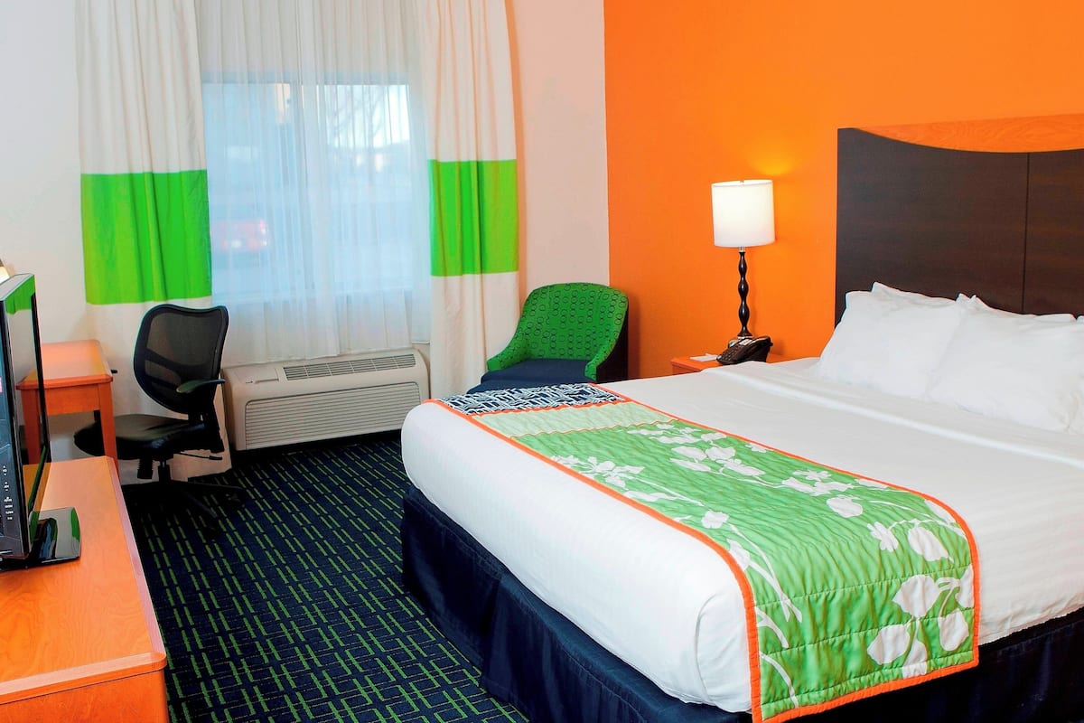 Habitación de hotel con cama, escritorio, silla, lámpara y ventana con cortinas.