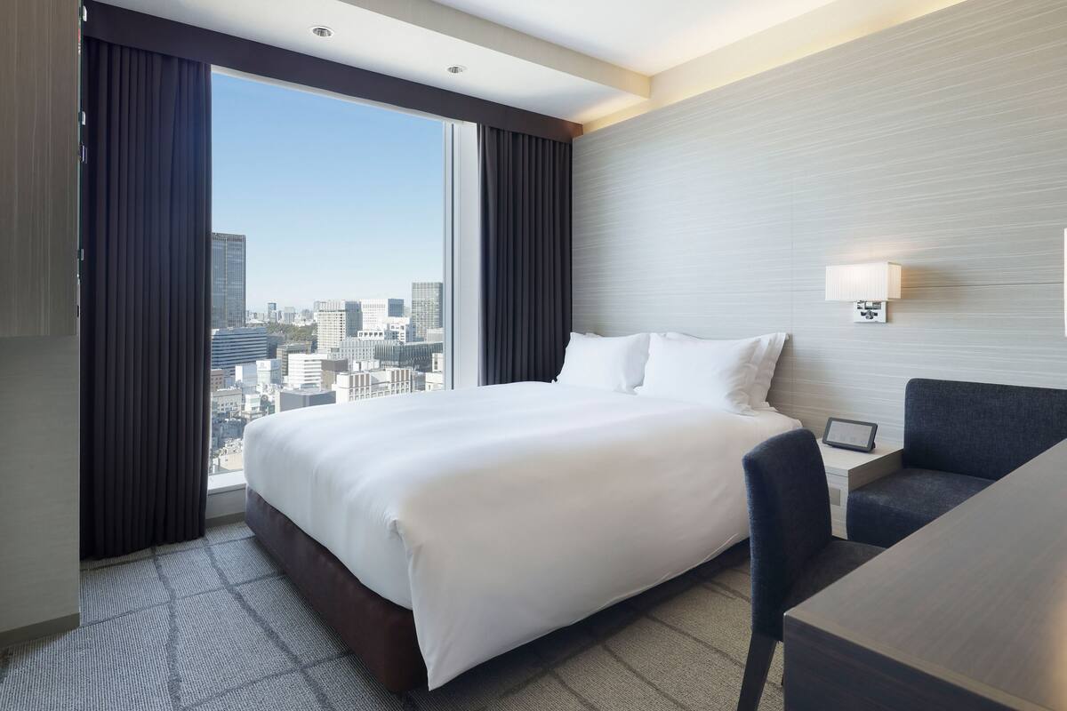 Une chambre d’hôtel dotée d’un grand lit, d’un bureau, d’une chaise, offrant une vue sur la ville et présentant un design moderne.
