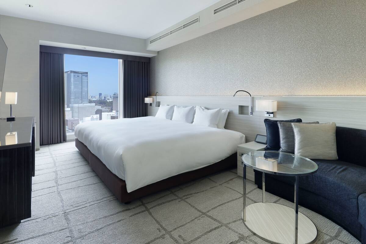 Une chambre d’hôtel avec un grand lit, une petite table ronde, un canapé et une vue sur le paysage urbain.