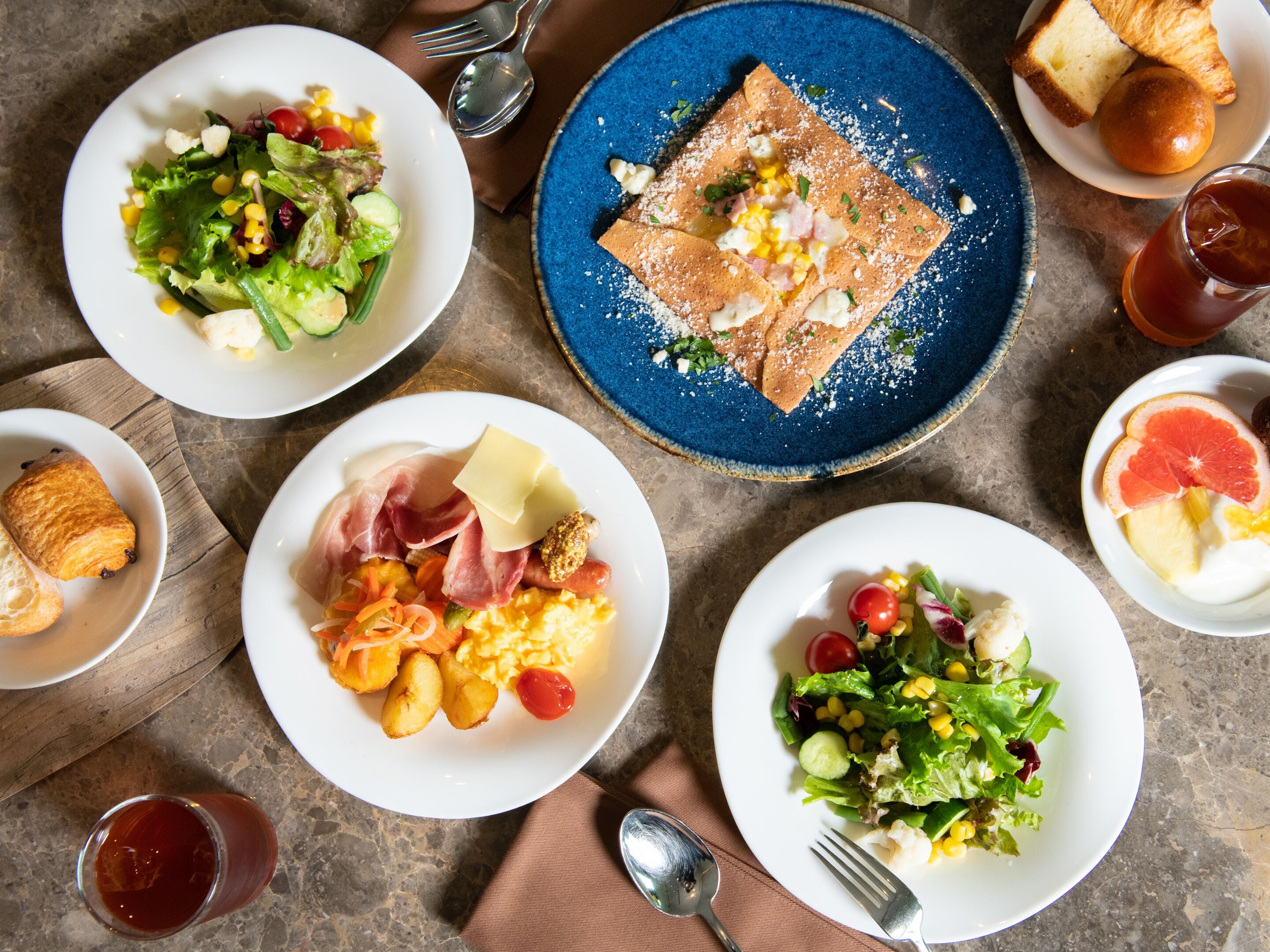 A variety of breakfast dishes on a table, including a plate of scrambled eggs, a salad, and a croissant.