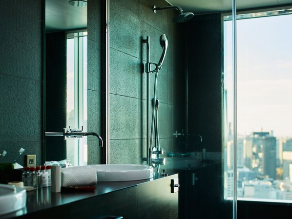 A modern bathroom with a large mirror, a glass shower enclosure, and a city view.