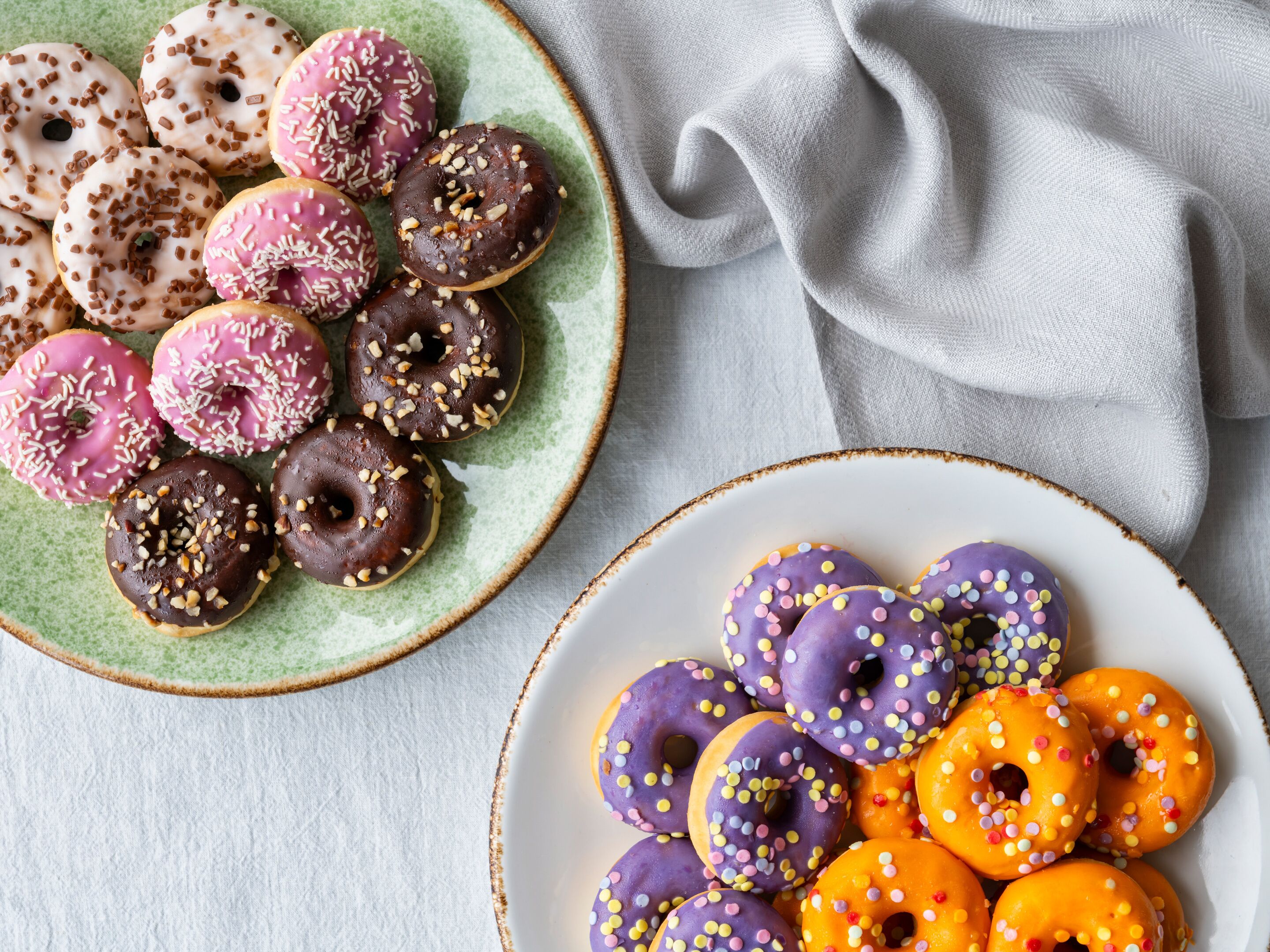 Two plates of assorted donuts with various toppings and colors.