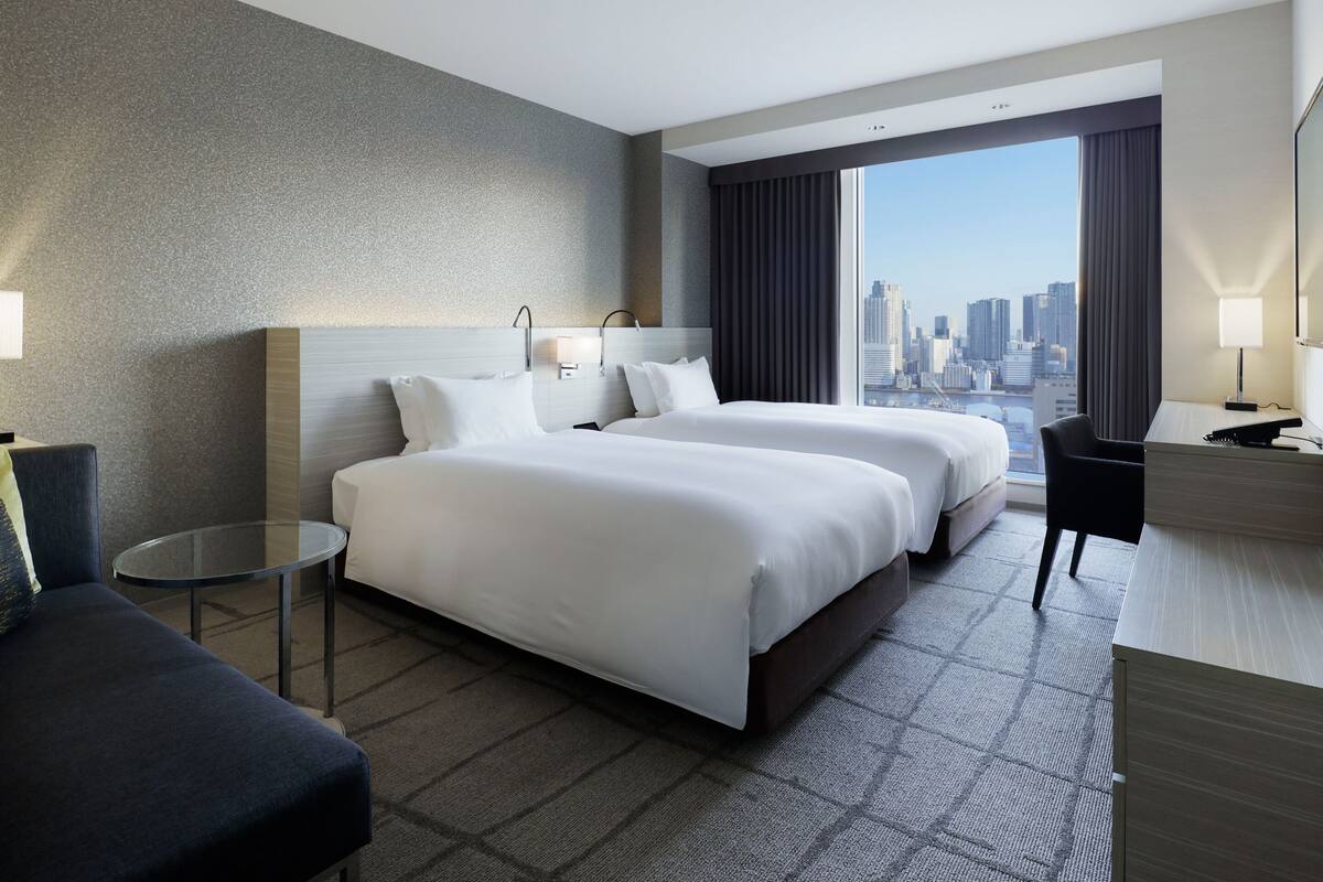 Une chambre d’hôtel avec deux lits, un bureau, une chaise, une table ronde et une vue sur la ville.