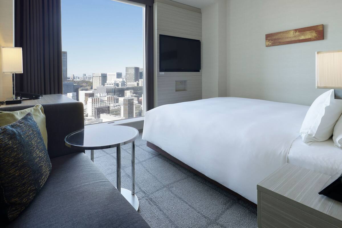Une chambre d’hôtel avec un lit, une petite table, un canapé, une télévision et une vue sur la ville.