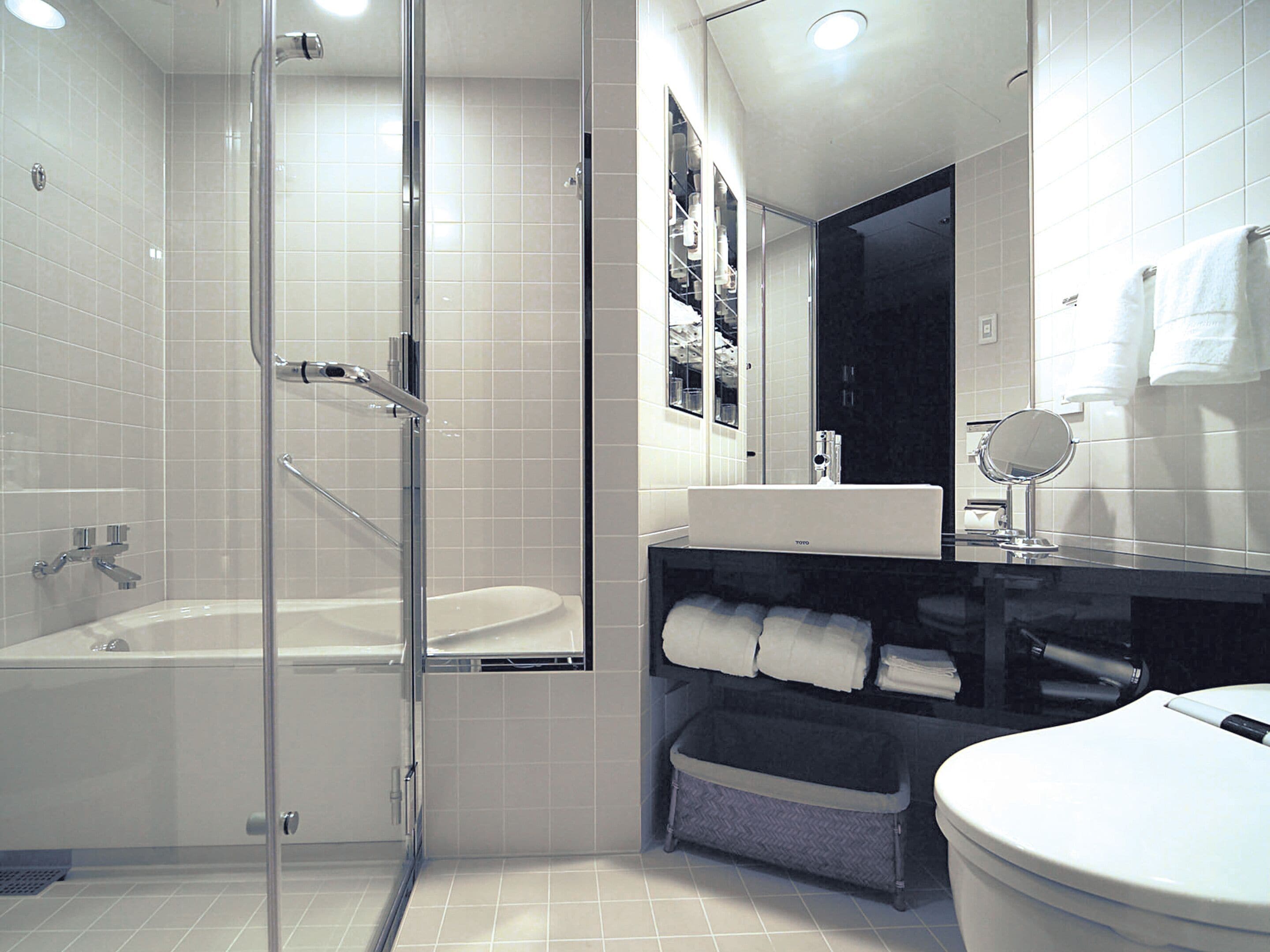 A modern bathroom with a glass-enclosed shower, a white bathtub, a vanity with a mirror, and a toilet.