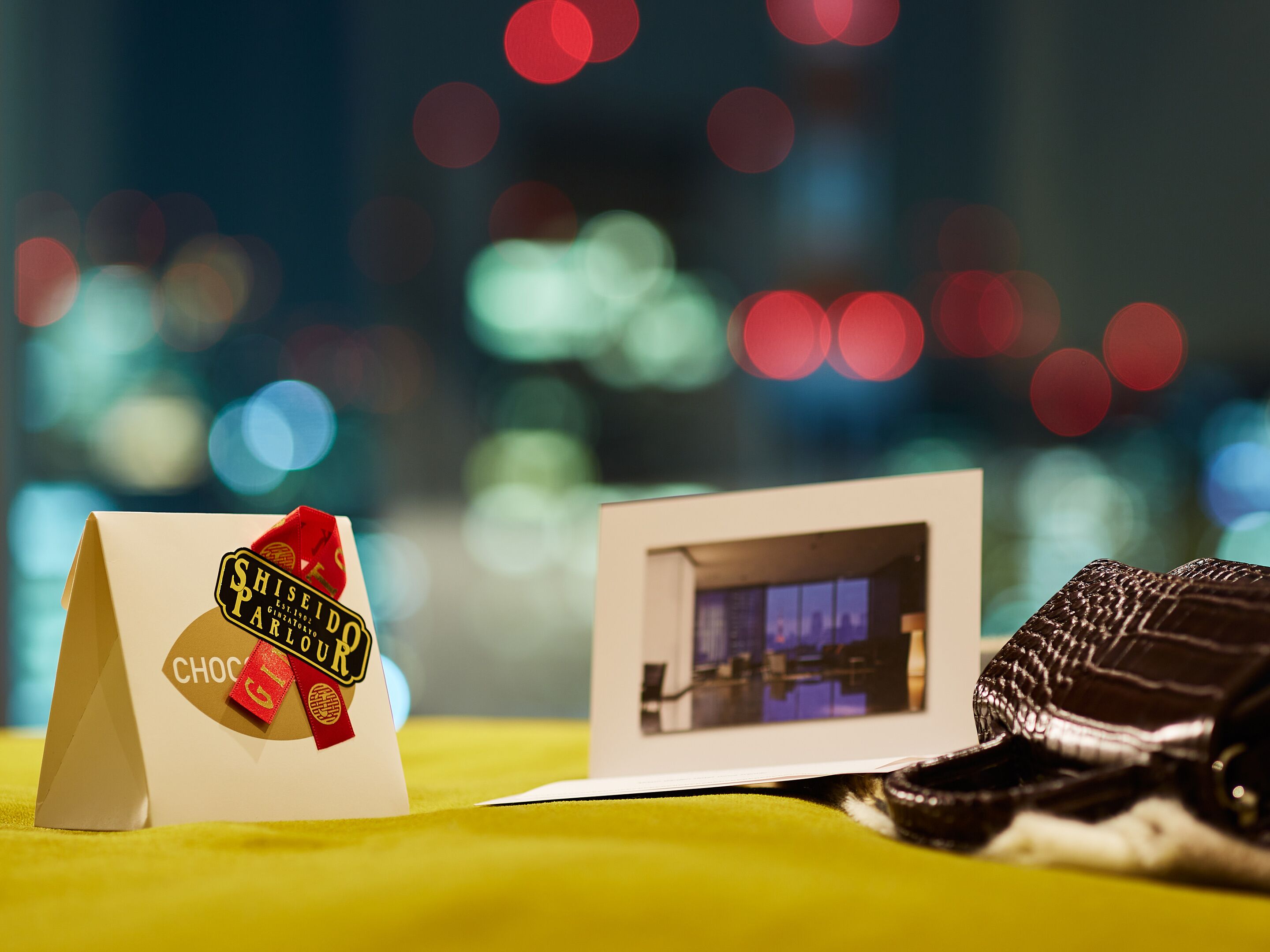A gift bag with a chocolate label, a photograph of a room, and a chocolate bar on a yellow surface.