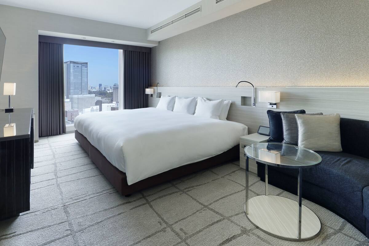 Une chambre d’hôtel avec un grand lit, une petite table, un canapé et une vue sur le paysage urbain.