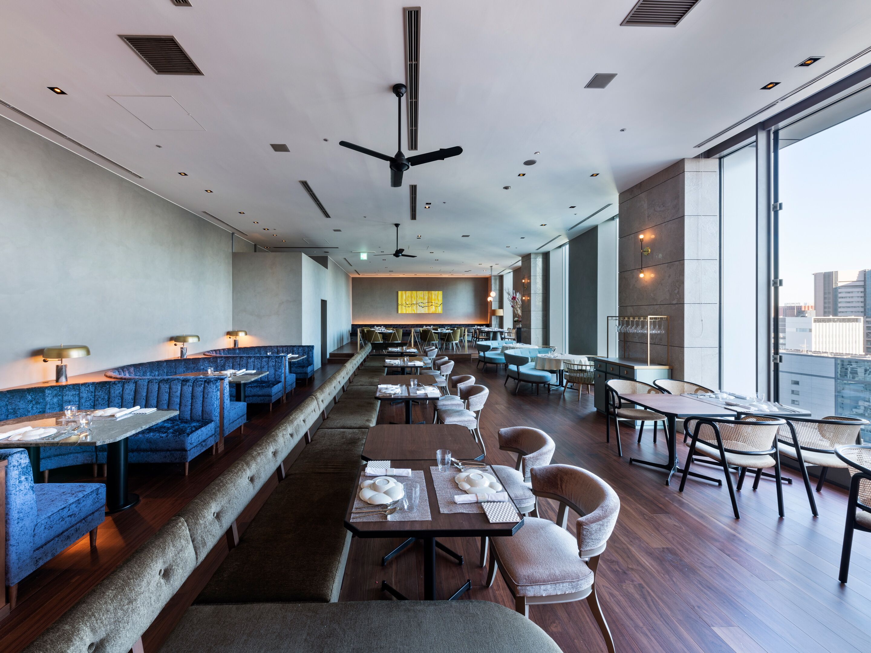 A modern restaurant with blue booths, wooden tables, and a high ceiling with a fan.