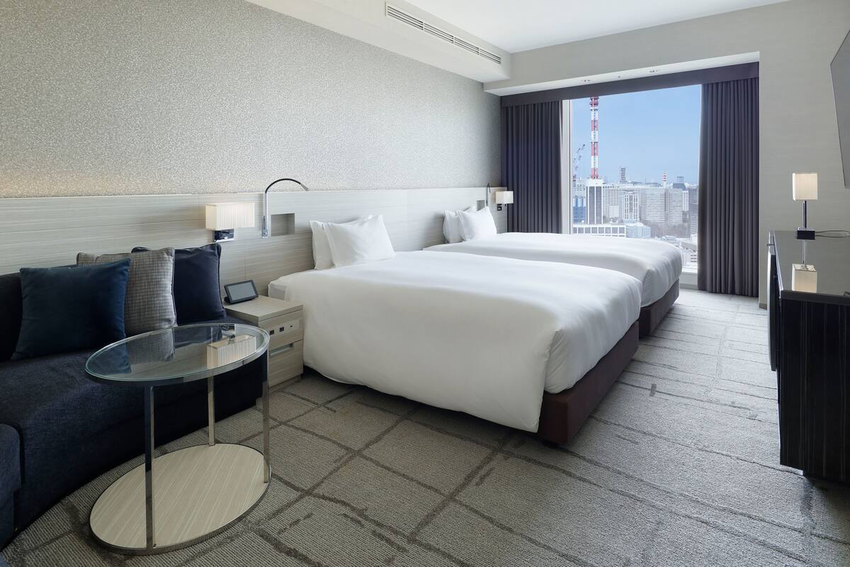 Une chambre d’hôtel avec deux lits, un canapé, une petite table et une vue sur le paysage urbain.