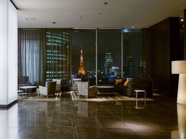 Un moderno vestíbulo de hotel con un amplio ventanal que ofrece una vista nocturna de la ciudad, incluyendo una torre destacada.