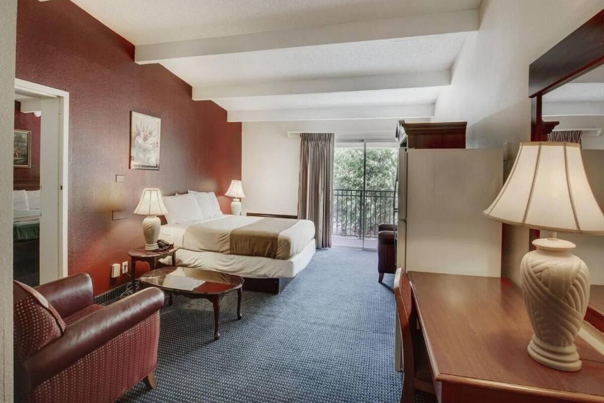 Quarto de hotel com cama, escrivaninha, cadeira, luminária e vista para o exterior.