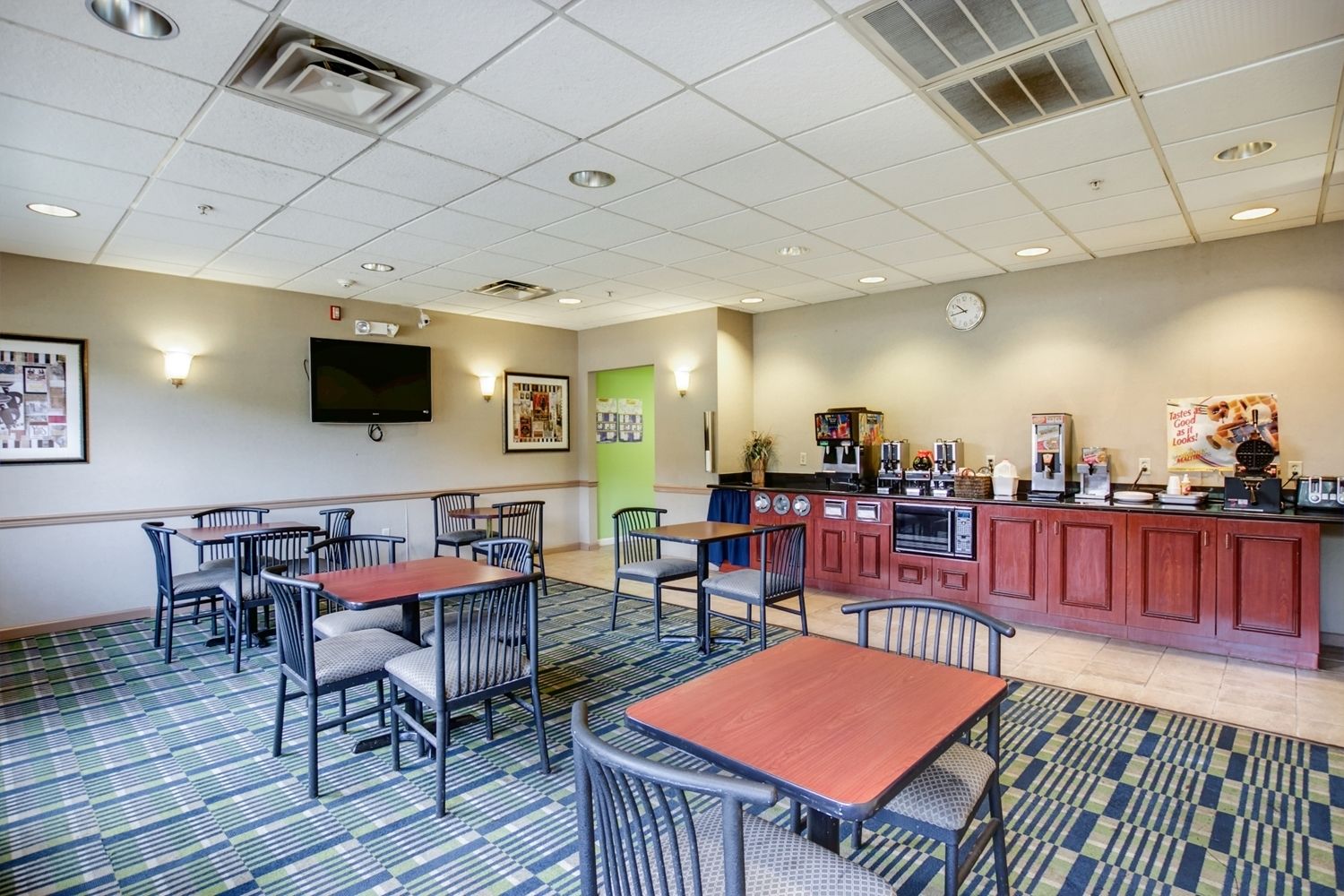 A hotel room with a kitchenette, a flat-screen TV, and a dining area with tables and chairs.