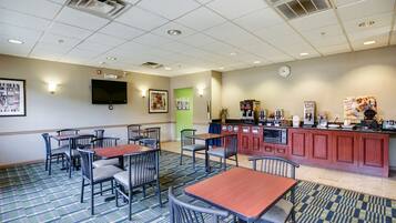 A hotel room with a kitchenette, a flat-screen TV, and a dining area with tables and chairs.